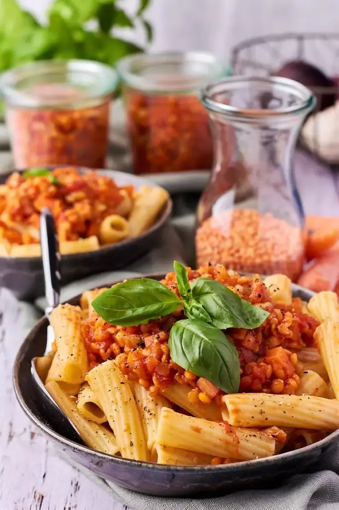 Schnelle Linsenbolognese mit roten Linsen auf Pasta, im Hintergrund Gläser mit Soße