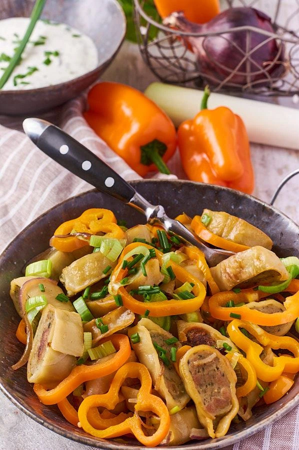 Zwei Portionen Maultaschen-Pfanne mit Gemüse auf Holztisch mit Besteck
