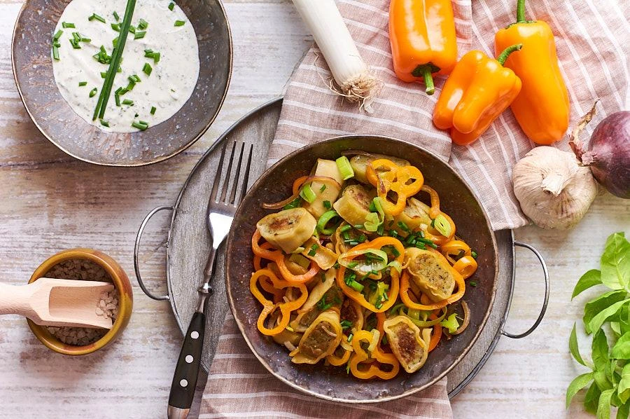 Maultaschen-Pfanne mit Gemüse auf grauen Teller mit frischem Schnittlauch serviert