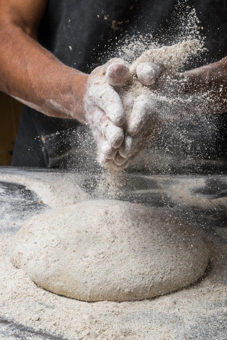 Hände kneten Brotteig mit Mehlstaub in der Luft