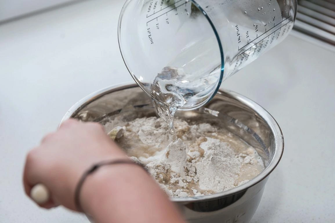 Wasser wird aus Messbecher in Mehlschüssel gegossen – Beginn des Brotteigs
