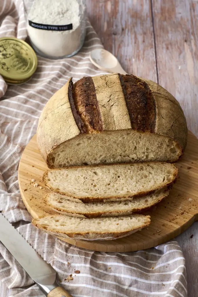 Erstes Sauerteigbrot angeschnitten auf Holzbrett mit Scheiben