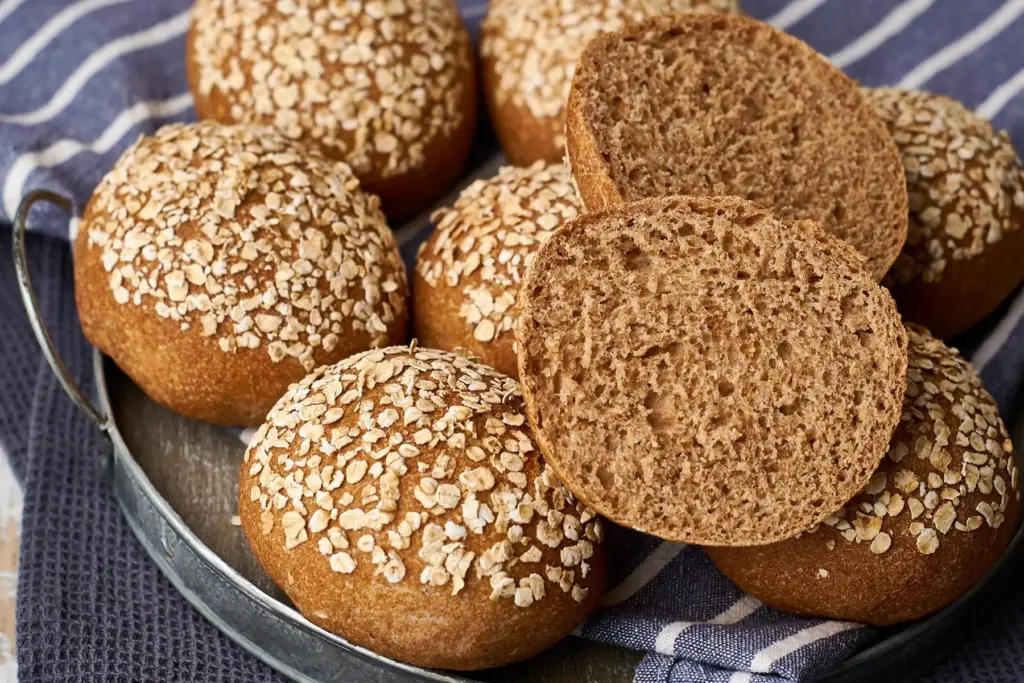 Dinkel-Vollkornbrötchen mit Haferflocken auf Metallteller, eines aufgeschnitten mit saftiger Vollkorn-Krume