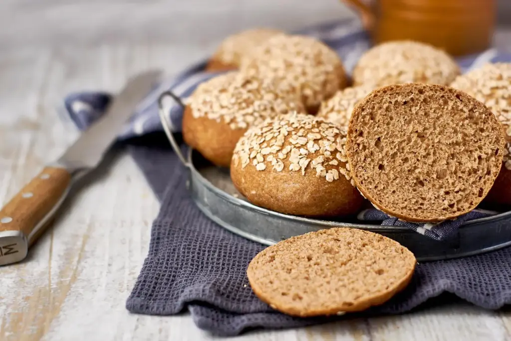 Dinkel-Vollkornbrötchen mit Haferflocken-Topping auf Metallteller mit blau-weiß gestreiftem Geschirrtuch