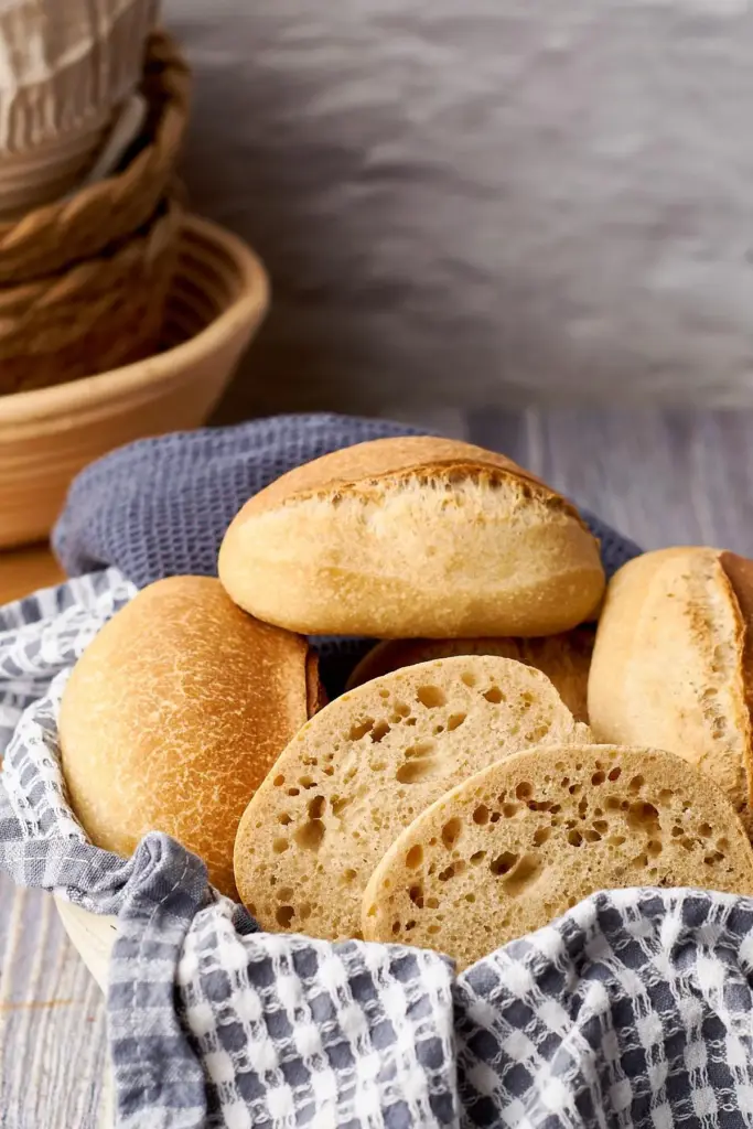 Sonntagsbrötchen mit goldbrauner Kruste im Teigtuch, aufgeschnittene Brötchenhälften zeigen lockere Krume
