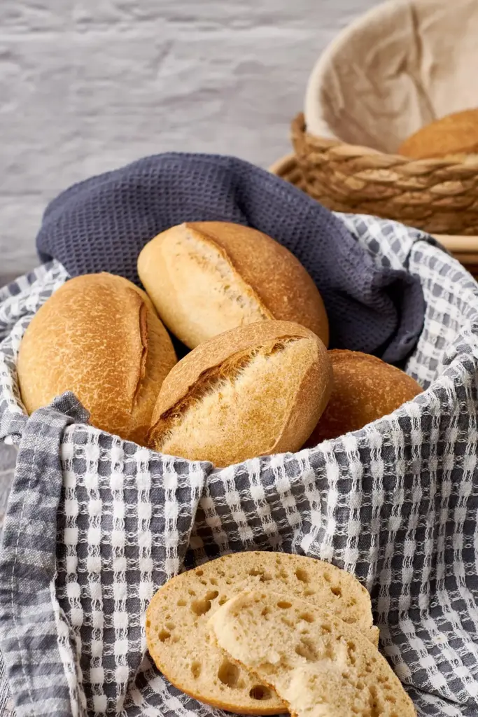 Knusprige Sonntagsbrötchen in Korb mit blau-weißem Teigtuch, zwei Hälften zeigen die luftige Krume