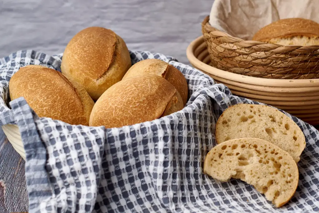 Sonntagsbrötchen mit Übernacht-Gare in Korb mit Teigtuch, eines aufgeschnitten zeigt luftige Krume