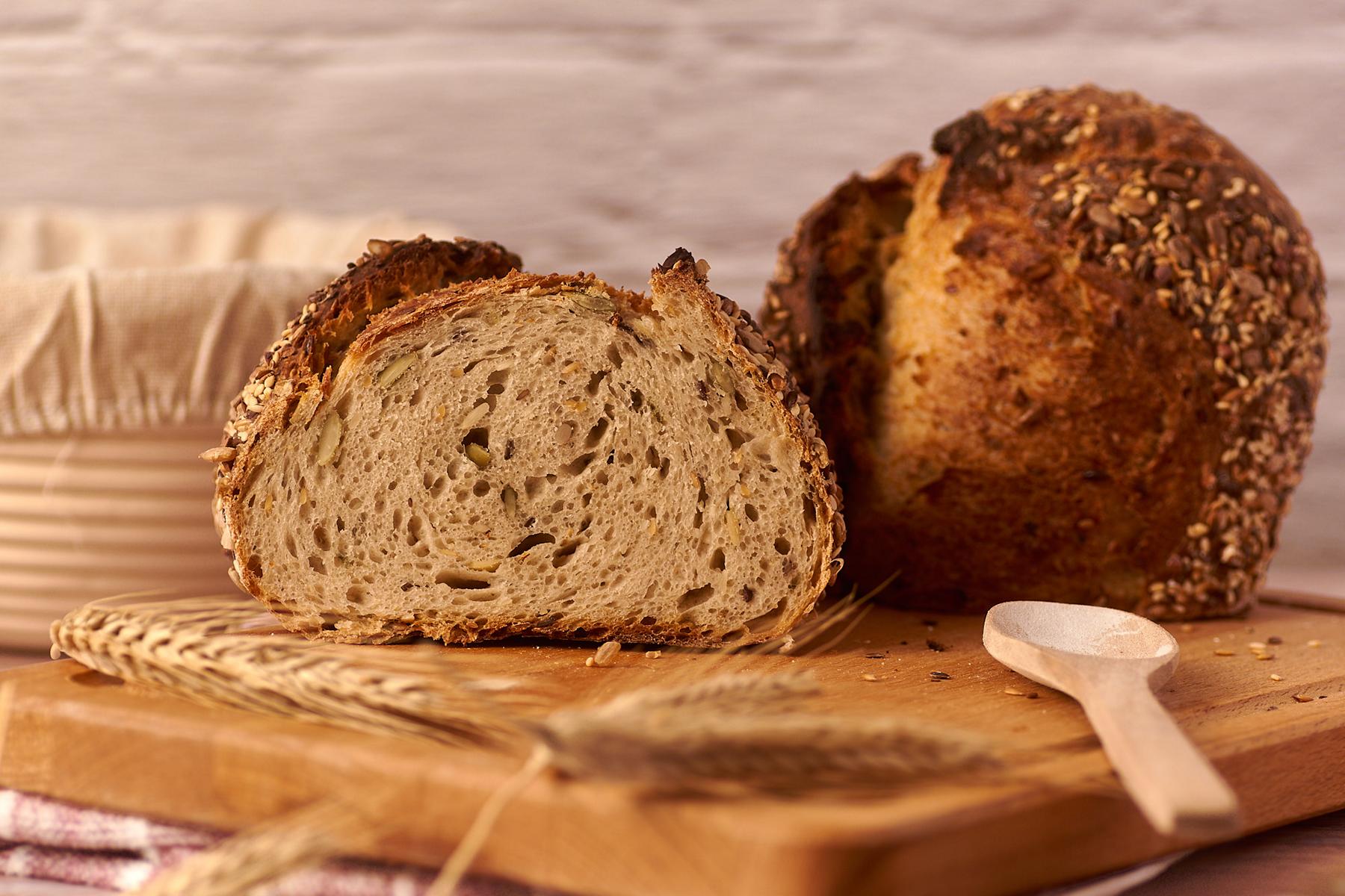 Saatenbrot mit Sauerteig angeschnitten auf dem Holzbrett, daneben Weizenähren