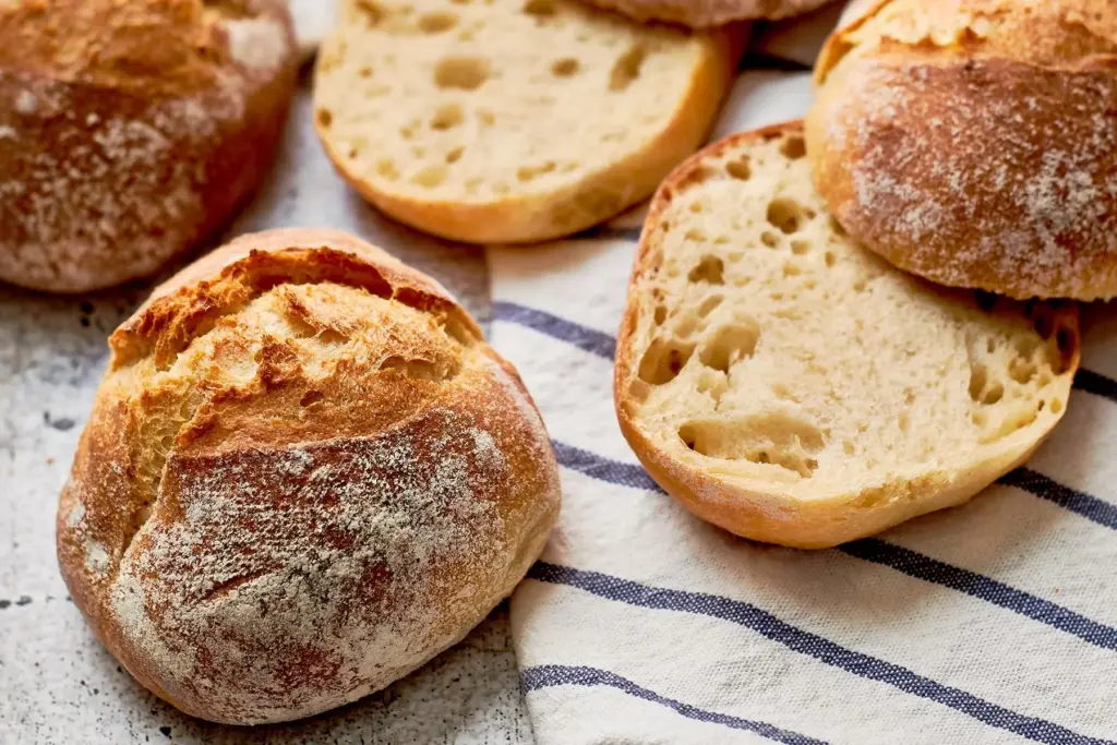 Einzelner Einkorn-Dinkel-Bobbel mit charakteristischem Ausbund, daneben aufgeschnittene Hälften