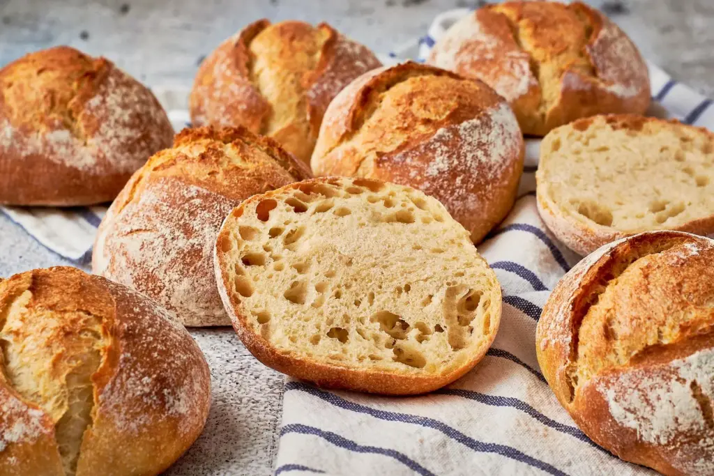 Frisch gebackene Einkorn-Dinkel-Brötchen auf Küchentuch, einer aufgeschnitten zeigt saftige Krume