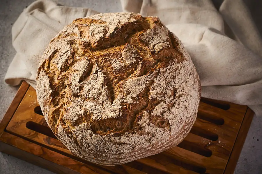 Rustikaler Schrotlaib mit bemehlter Kruste auf Holzbrett – Weizenmischbrot backen mit Röst-Brühstück