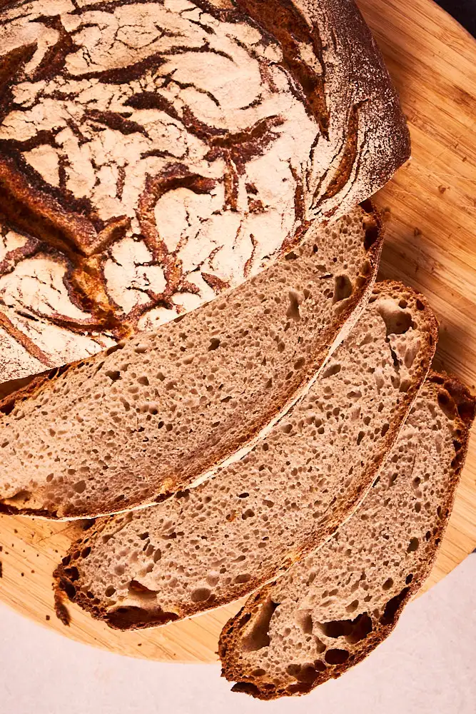 Angeschnittenes Roggen-Weizen-Sauerteigbrot mit Scheiben auf einem Holzbrett