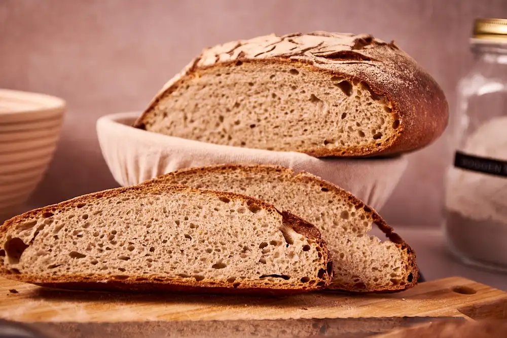 Sauerteigbrot für Anfänger in Scheiben, dahinter der Laib im Gärkörbchen