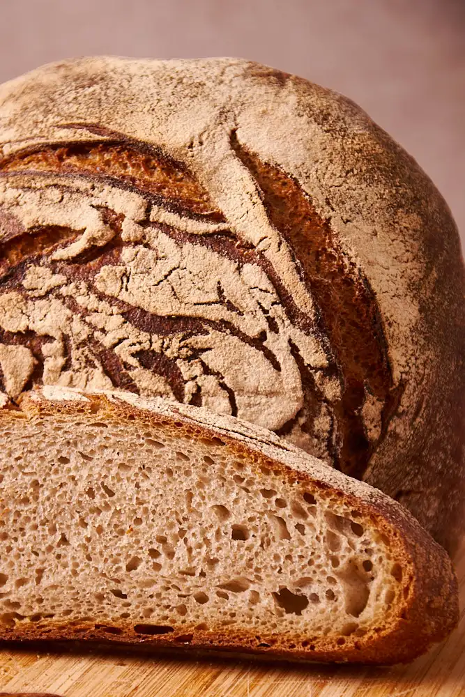 Rundes Sauerteigbrot ohne Hefe mit bemehlter, aufgerissener Kruste und angeschnittener Krume