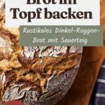 Rustikal aufgerissener Laib Dinkel-Roggen-Brot mit Mehlkruste auf einem Holzbrett