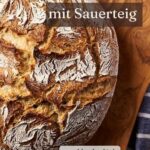 Rustikal aufgerissene Mehlkruste eines runden Bauernbrots auf einem Holzbrett in Nahaufnahme