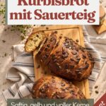 Zwei Laibe Kürbisbrot mit Sauerteig und Kürbiskern-Kruste auf einem Holzbrett, der obere angeschnitten