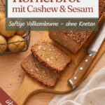 Angeschnittenes Körnerbrot aus der Kastenform mit Sesamkruste auf einem Holzbrett, daneben ein Messer und ein Korb Kartoffeln